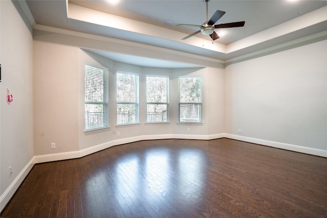 spare room with a tray ceiling, baseboards, ceiling fan, and dark wood finished floors