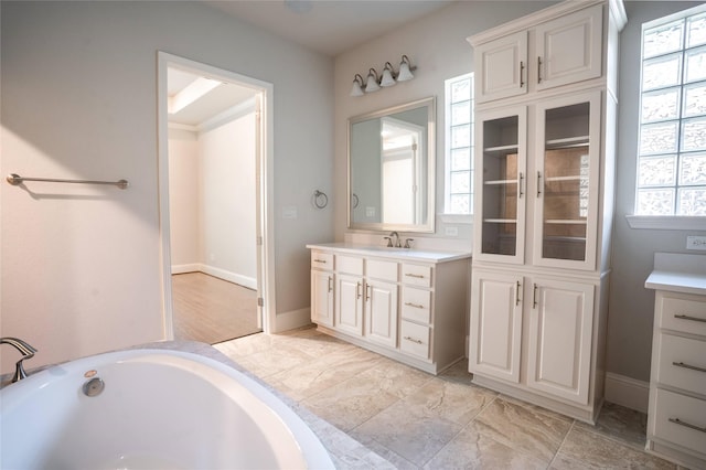 full bath with baseboards, a bathing tub, and vanity