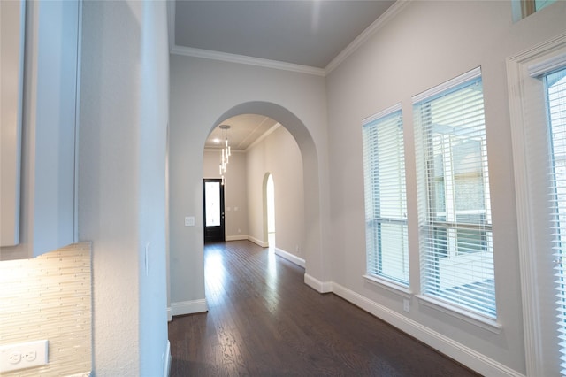 hallway with arched walkways, crown molding, baseboards, and dark wood-style flooring