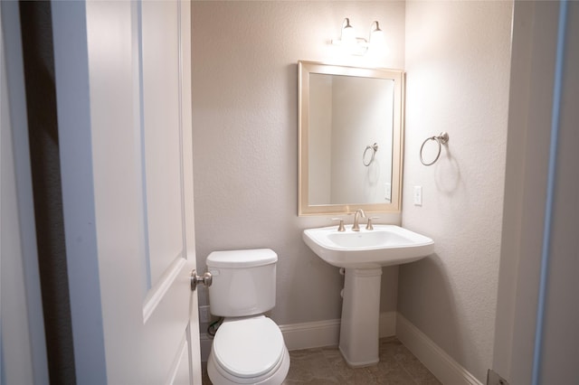 half bath with baseboards, toilet, and tile patterned flooring