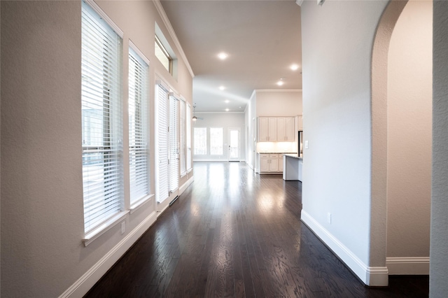 hallway featuring baseboards, arched walkways, dark wood-style flooring, and ornamental molding