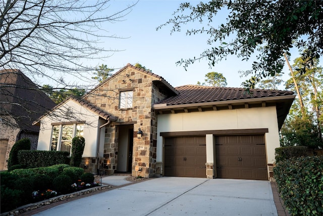 mediterranean / spanish-style house with stucco siding, driveway, stone siding, an attached garage, and a tiled roof