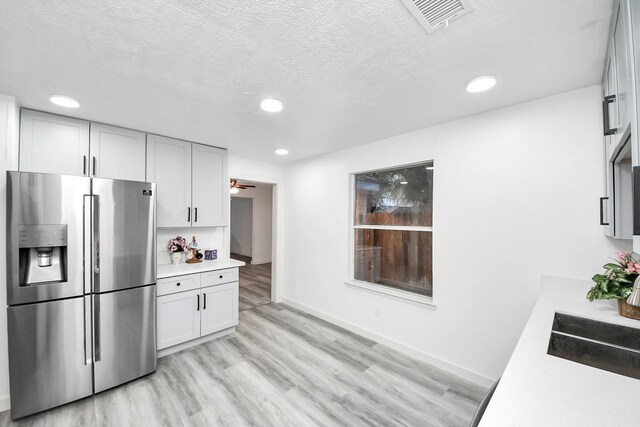 kitchen featuring light wood-type flooring, visible vents, stainless steel refrigerator with ice dispenser, a textured ceiling, and light countertops