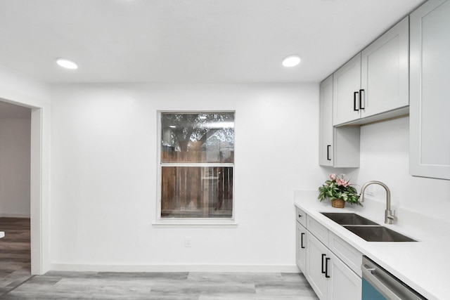 kitchen featuring a sink, baseboards, light countertops, light wood-style floors, and stainless steel dishwasher