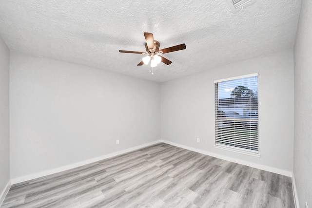 empty room with a ceiling fan, visible vents, light wood finished floors, baseboards, and a textured ceiling