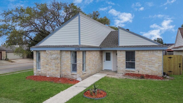 view of front of property with brick siding, roof with shingles, a front lawn, and fence