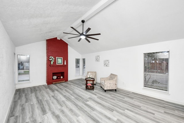 unfurnished room with wood finished floors, baseboards, lofted ceiling with beams, ceiling fan, and a brick fireplace