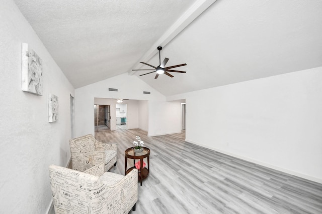 living area featuring a ceiling fan, visible vents, light wood finished floors, lofted ceiling with beams, and a textured ceiling