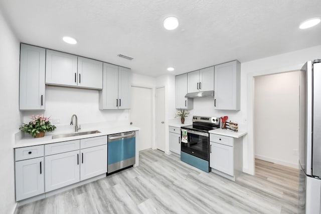 kitchen with light wood-type flooring, a sink, under cabinet range hood, appliances with stainless steel finishes, and light countertops