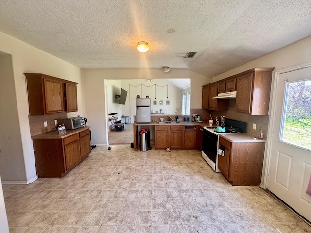 kitchen with under cabinet range hood, gas stove, brown cabinetry, and a sink