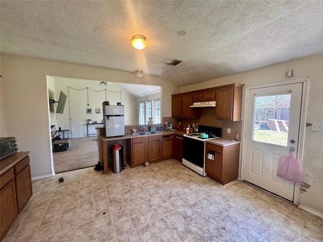 kitchen featuring visible vents, under cabinet range hood, brown cabinets, freestanding refrigerator, and electric range