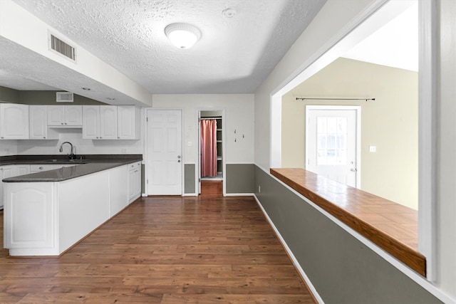 kitchen with visible vents, dark wood finished floors, a sink, white cabinetry, and dark countertops