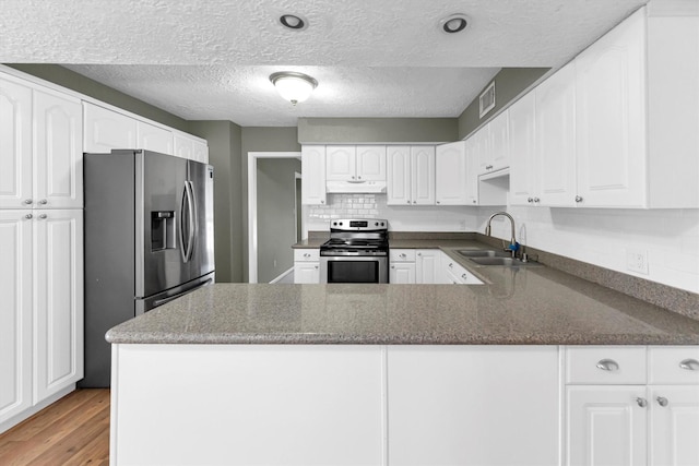 kitchen with a sink, under cabinet range hood, stainless steel appliances, light wood-style floors, and a peninsula