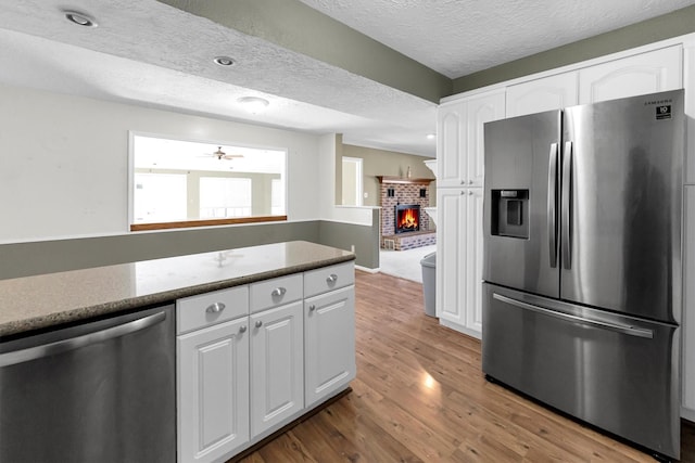 kitchen featuring white cabinets, a brick fireplace, stainless steel appliances, and wood finished floors