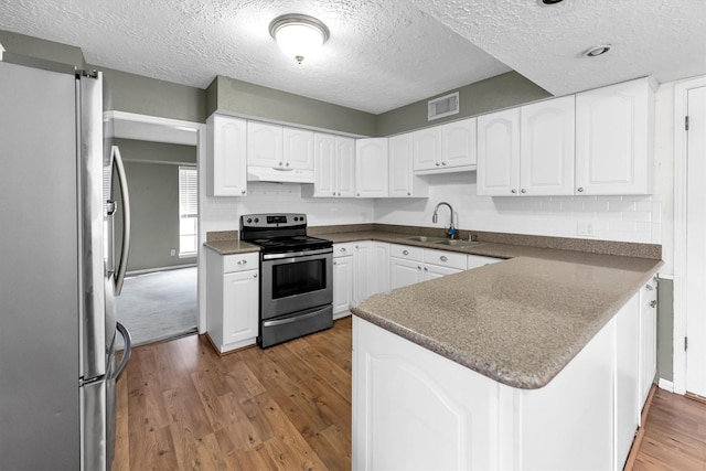 kitchen featuring visible vents, under cabinet range hood, wood finished floors, stainless steel appliances, and a sink