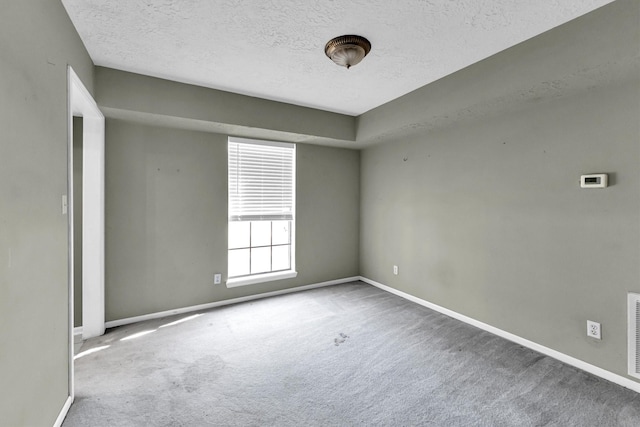 carpeted spare room with visible vents, baseboards, and a textured ceiling