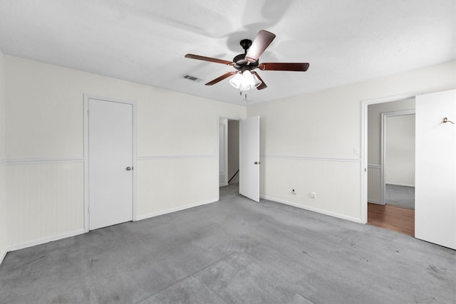 unfurnished bedroom with a wainscoted wall, carpet, visible vents, and ceiling fan