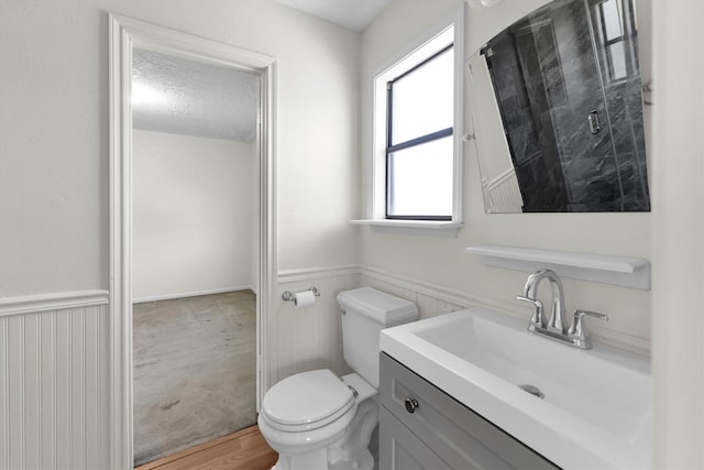 bathroom with a shower stall, toilet, vanity, wainscoting, and a textured ceiling