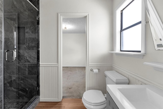 full bath with wood finished floors, a stall shower, wainscoting, a textured ceiling, and toilet