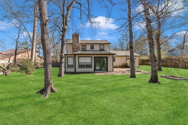 rear view of house with a yard, a fenced backyard, french doors, and a chimney