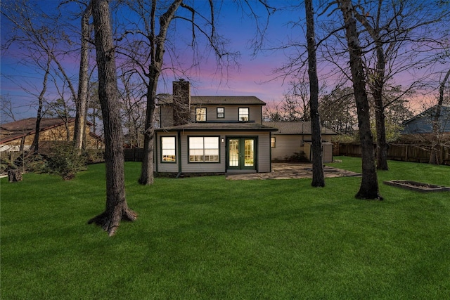 back of property at dusk featuring fence, french doors, a lawn, and a chimney