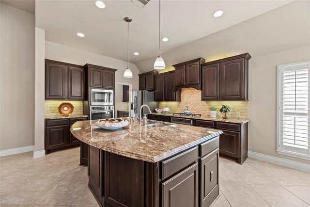 kitchen with a kitchen island with sink, a sink, stainless steel appliances, dark brown cabinetry, and pendant lighting