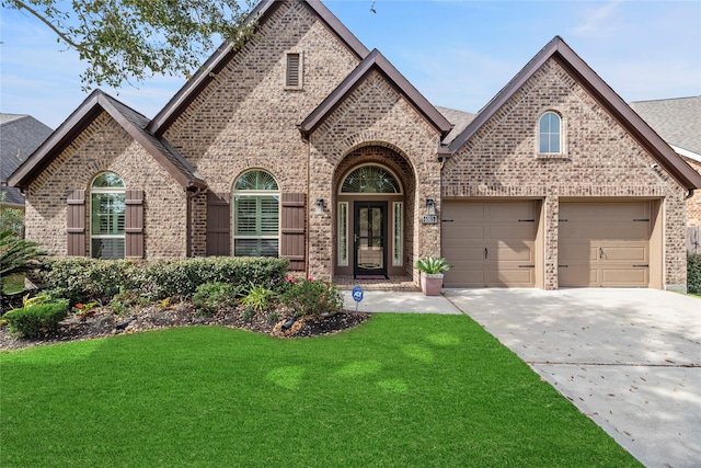 french country home featuring brick siding, a garage, concrete driveway, and a front lawn