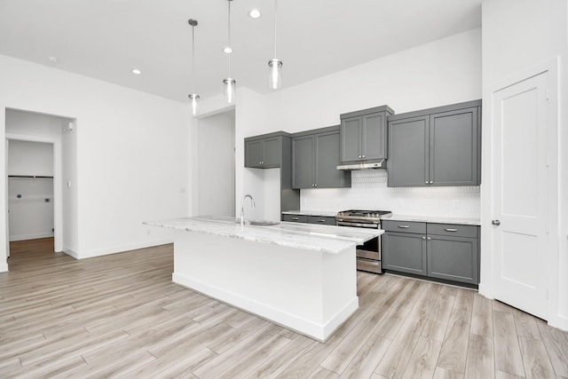 kitchen with under cabinet range hood, light wood-style flooring, stainless steel range with gas stovetop, and gray cabinets