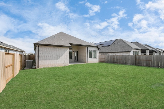 back of property with brick siding, a fenced backyard, a lawn, and central AC