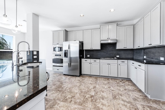 kitchen with under cabinet range hood, backsplash, appliances with stainless steel finishes, and a sink