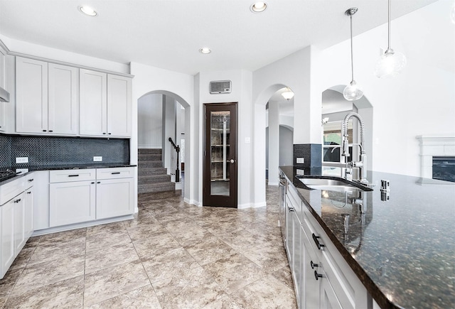 kitchen with a sink, decorative backsplash, arched walkways, and dark stone countertops