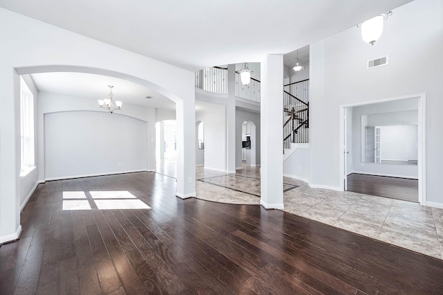 unfurnished living room with hardwood / wood-style floors, visible vents, baseboards, a high ceiling, and arched walkways