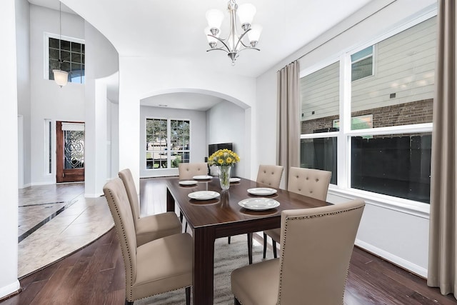 dining space featuring baseboards, wood finished floors, arched walkways, and a chandelier