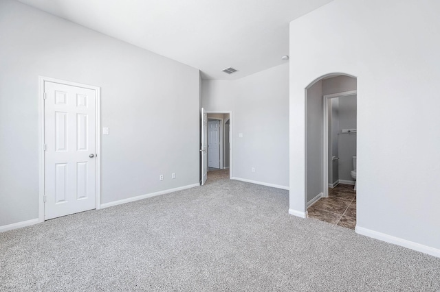 unfurnished bedroom with visible vents, connected bathroom, baseboards, carpet flooring, and arched walkways