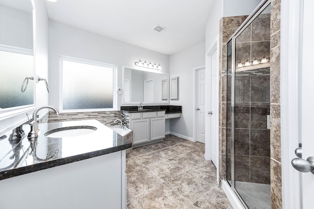 full bath featuring visible vents, a shower stall, two vanities, and a sink