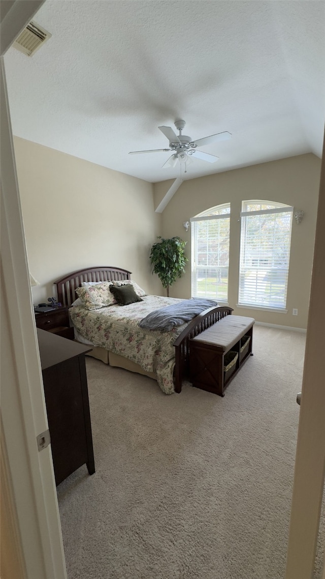 carpeted bedroom featuring a textured ceiling, lofted ceiling, visible vents, and ceiling fan