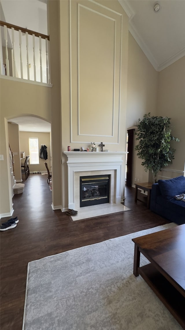 living room featuring arched walkways, high vaulted ceiling, ornamental molding, and a fireplace with flush hearth