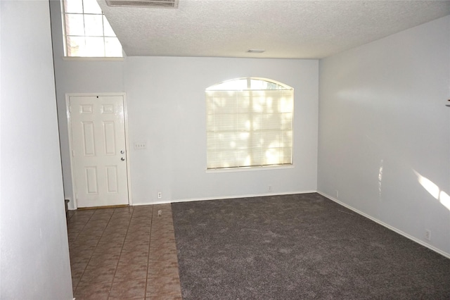 tiled empty room featuring visible vents, baseboards, a textured ceiling, and carpet