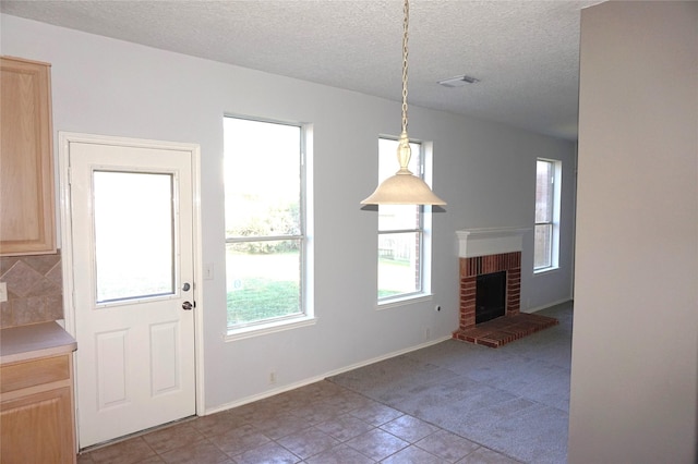 unfurnished dining area with a brick fireplace, baseboards, visible vents, and a textured ceiling