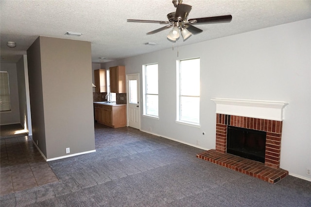 unfurnished living room with baseboards, a brick fireplace, a textured ceiling, and ceiling fan