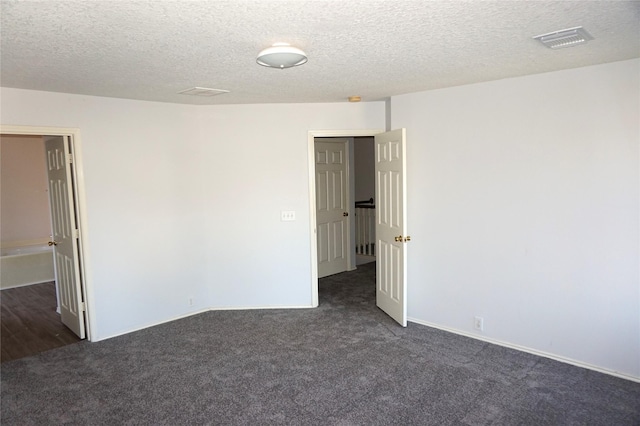 empty room with visible vents, dark colored carpet, and a textured ceiling