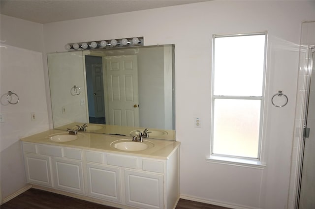 bathroom with double vanity, wood finished floors, a shower, and a sink