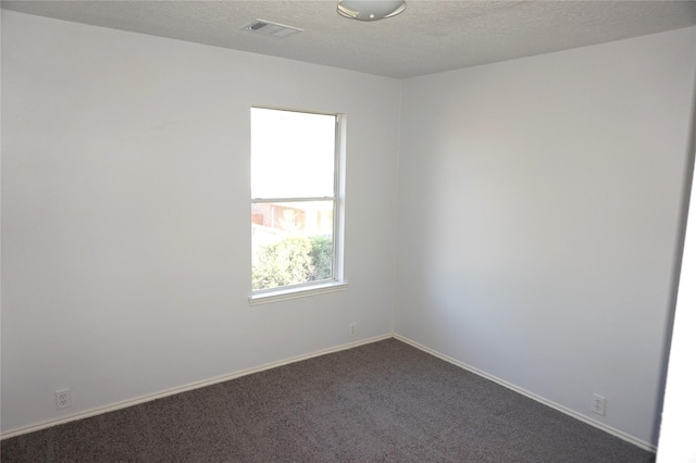 unfurnished room featuring visible vents, baseboards, a textured ceiling, and dark carpet