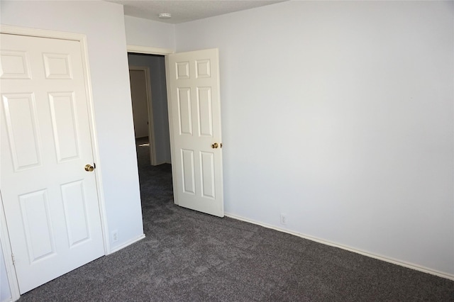 unfurnished bedroom featuring baseboards and dark colored carpet