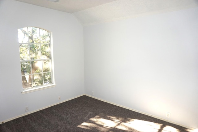 unfurnished room featuring lofted ceiling, a wealth of natural light, baseboards, and dark carpet