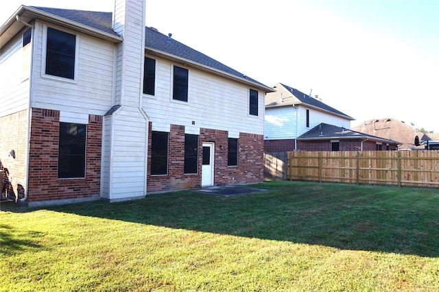 back of property featuring a chimney, fence, brick siding, and a lawn