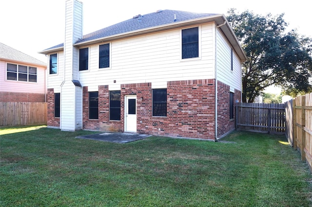 back of house with a yard, a fenced backyard, brick siding, and a chimney