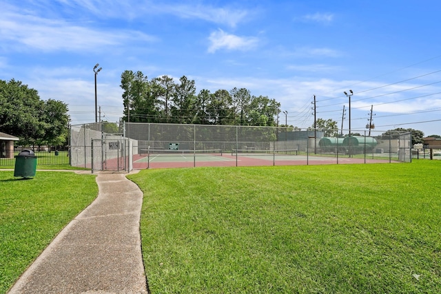 view of tennis court featuring a lawn and fence