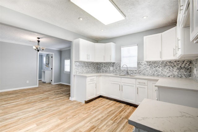 kitchen featuring a sink, tasteful backsplash, light wood-style flooring, and white cabinetry