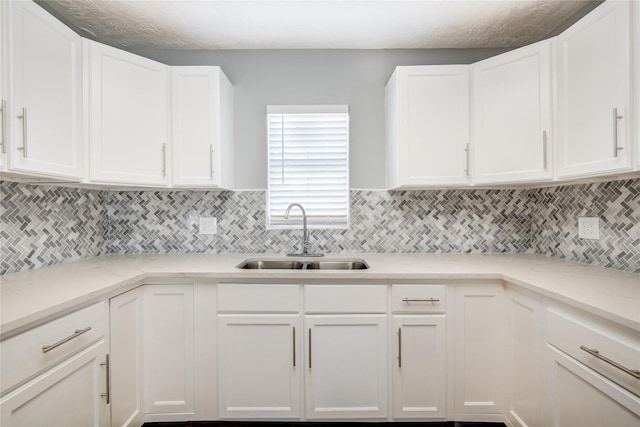 kitchen featuring light stone counters, decorative backsplash, white cabinetry, and a sink